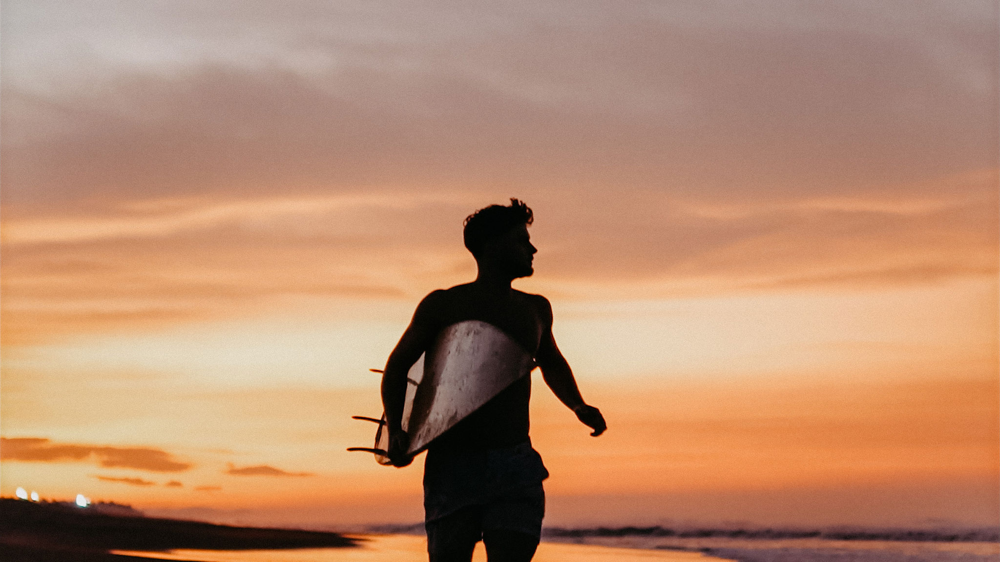 Surfer walking into the water at sunset in Bali